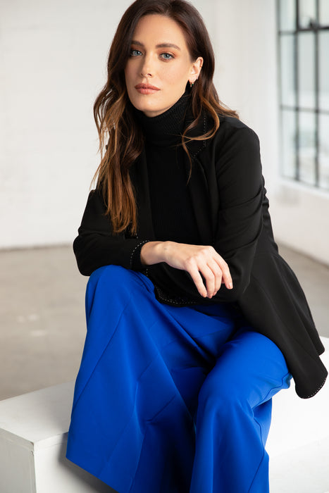 Woman in a sophisticated black turtleneck and blue trousers seated elegantly at Sunrise Studio, Apex Photo Studios' Studio D