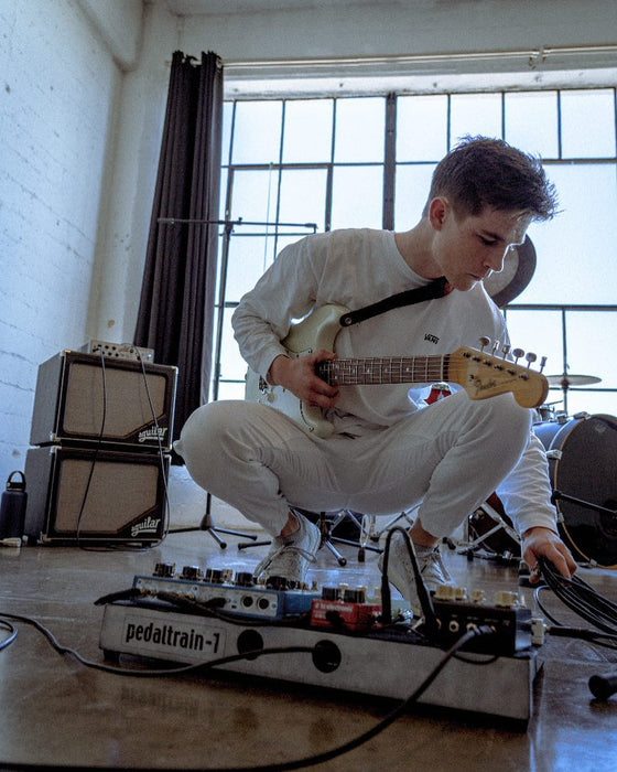 Musician tuning guitar effects pedals at Sunrise Studio, Apex Photo Studios' Studio D, with natural light from window