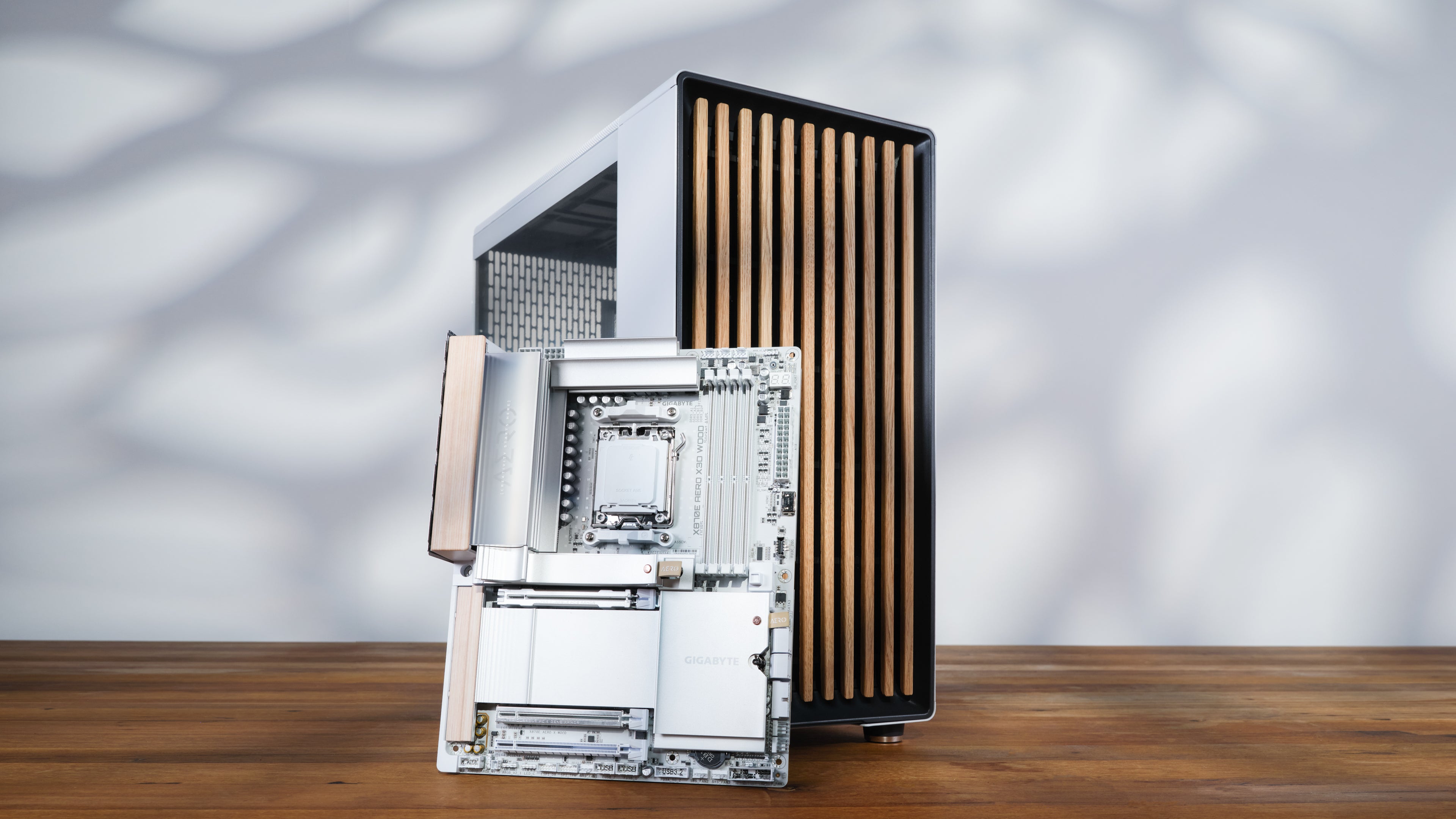 apex photo studios X870E AERO X3D Wood motherboard leaning on Fractal Design North XL Wood Chassis on wooden surface with white background and shadows that look like leaves.